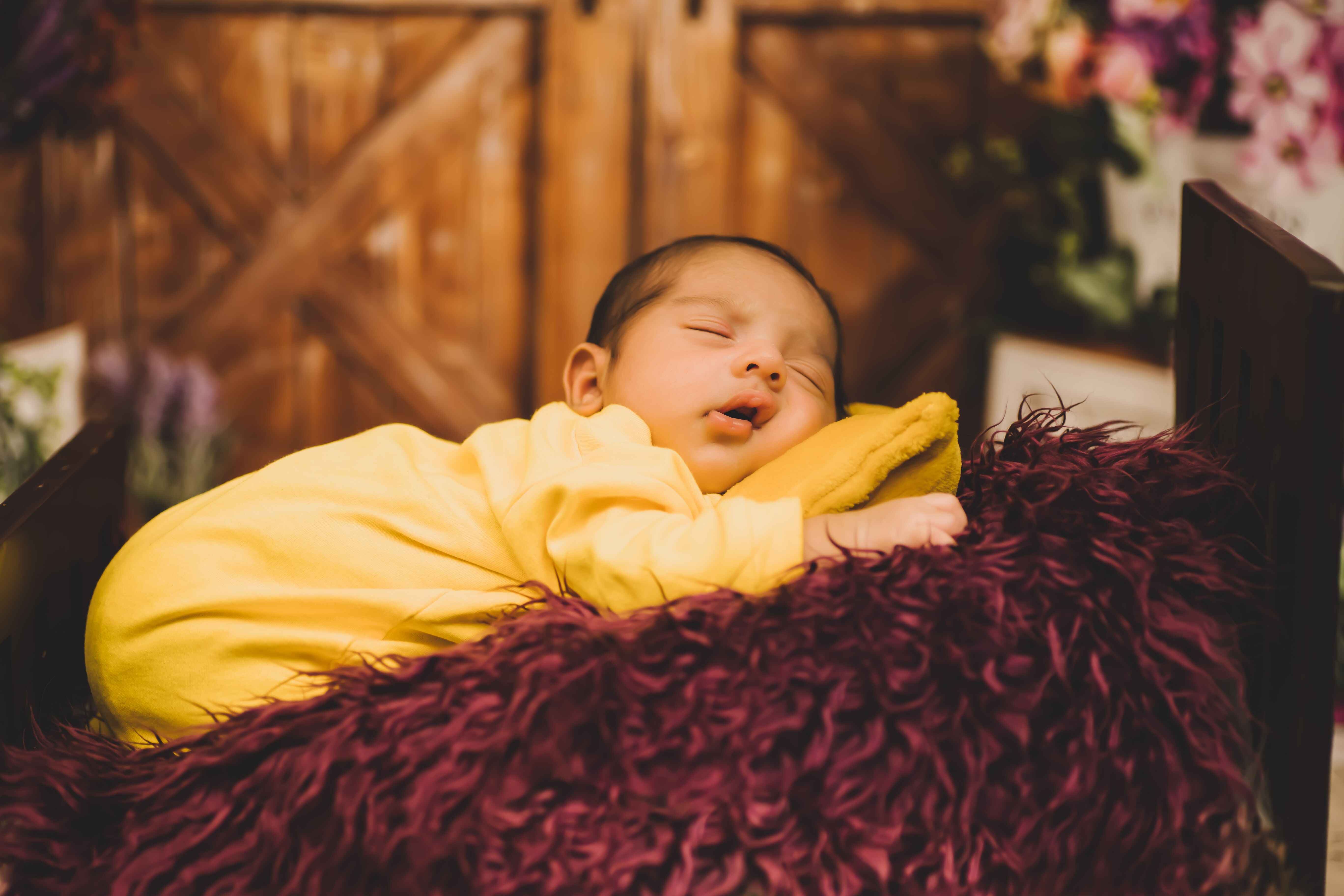 A baby peacefully asleep on a fur pillow, in a yellow dress, for an enchanting baby photoshoot.